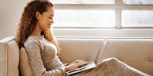 Woman sat on the sofa, working on a laptop. 