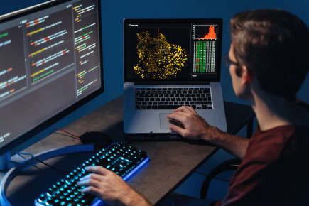 A man typing on a pc and laptop with programming code on screen