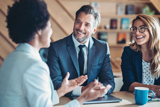 A man and a woman listen to another woman talking at a business meeting