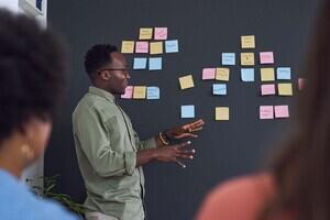 A man in a green shirt stands next to a dark wall full of colourful post-it notes.