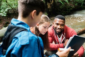 A group of people outside near a stream looking at a clipboard