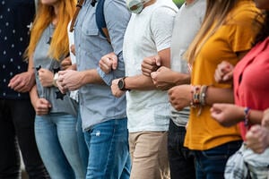 Group of young male and female protestors with arms in arms and clenching fist while standing together outdoors