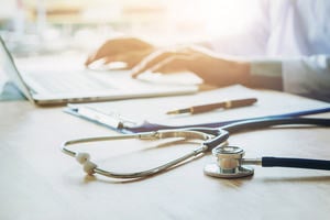 Person writing on a laptop next to a stethoscope