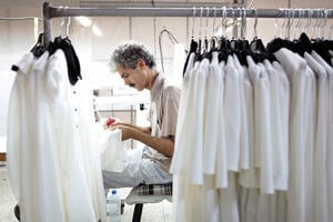 A man working on some textiles with clothes hanging beside him.