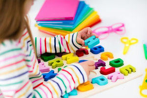 Young girl picking up a blue letter H from a coloured alphabet puzzle.