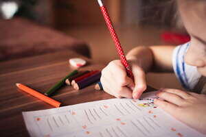 Autistic young student drawing on a worksheet with a few coloured pencils in an inclusive classroom.